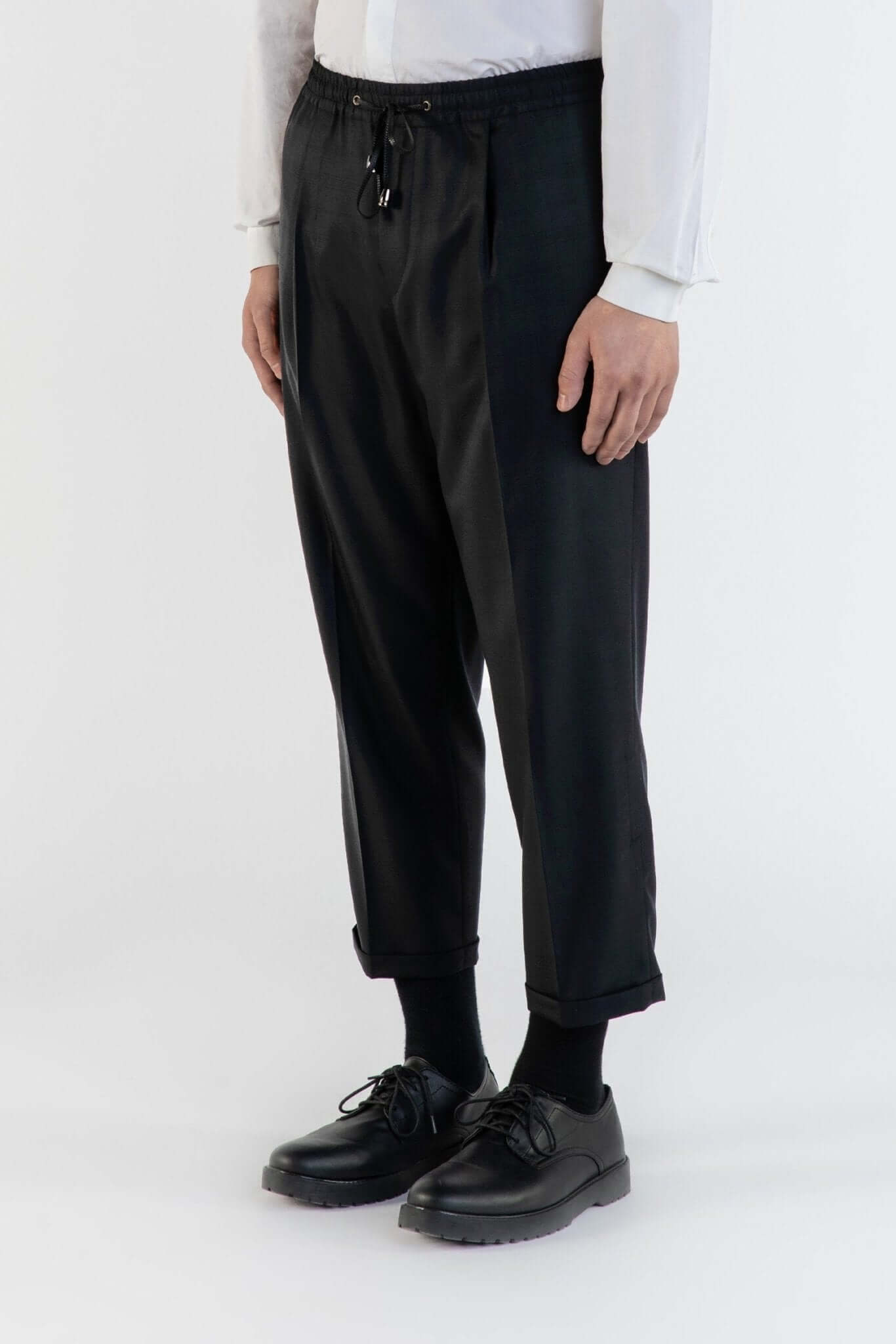 LE PANTALON NOIR À PLIS & CEINTURE ÉLASTIQUÉE EN LAINE porté par un modèle avec une chemise blanche.