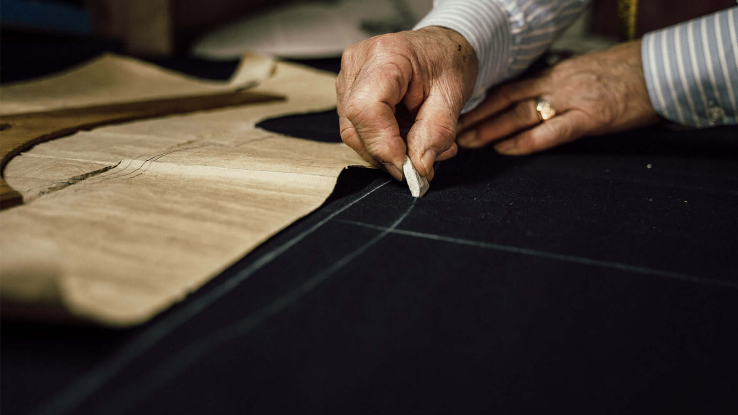 Tailor marking fabric with chalk next to a wooden pattern on a workspace for garment creation.