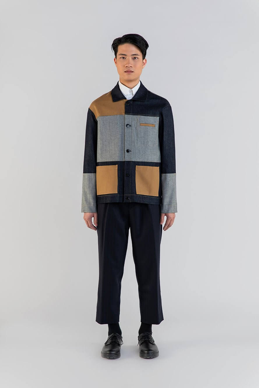 Homme portant un vêtement patchwork élégant avec pantalon noir à plis, ceinture élastique en laine, style moderne.