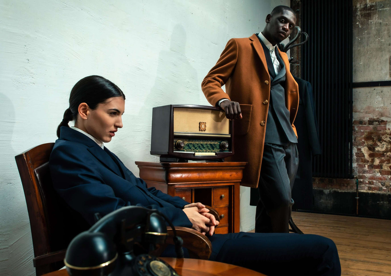 Stylish man and woman in vintage-inspired suits, posed in a retro office setting with an antique radio.